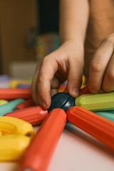 Obraz premium Close-up of a child’s hands building with colorful magnetic construction toys. Focus on motor skills development and creative play in a home environment