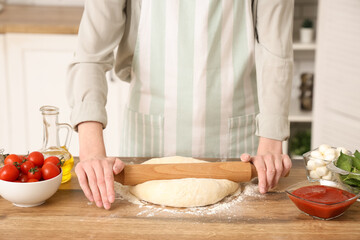 Woman rolling dough for pizza near table in kitchen