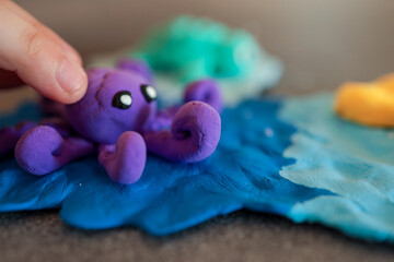 Children playing with colorful sea animals made from modeling clay, including a purple octopus, green fish, yellow starfish, and a red volcano on a blue ocean base
