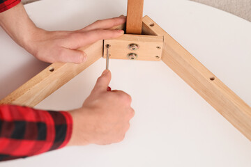 Male carpenter tightening screw in wooden table with screwdriver, closeup