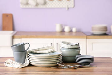 Clean plates, cutlery, bowls and cups on wooden counter in kitchen, closeup