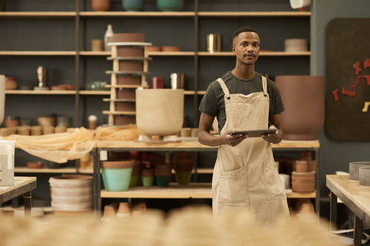 Young African potter working on a tablet in a large ceramics workshop