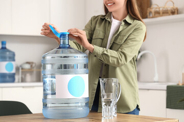 Woman opening bottle of clean water on table in kitchen