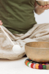 A man in a meditative pose uses a Tibetan singing bowl, gently tapping it with a soft hammer. The...