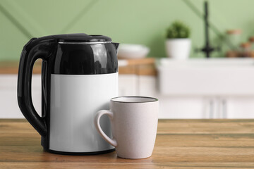 Modern electric kettle and cup on wooden table in kitchen