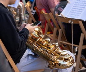 Man checking the phoen while playing the saxophone in a orchestra. Distraction