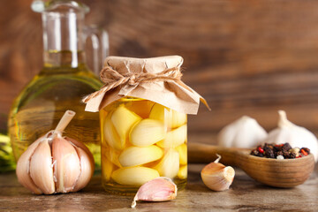 Jug and jar of fresh garlic oil with peppercorns on wooden background