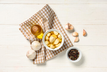 Bottle and bowl of fresh garlic oil with peppercorns on white wooden background