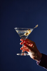 Hand holding martini glass garnished with olives against a blue background creating an elegant and...