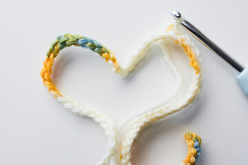 Colorful crochet hook with heart shaped yarn on white background