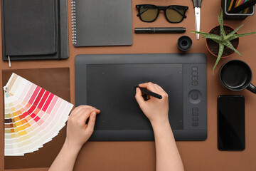 Female graphic designer working with tablet on brown background, top view