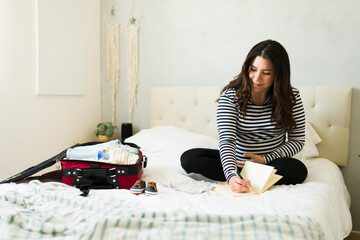 Cute pregnant woman preparing hospital bag, writing checklist while smiling comfortably at home