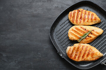 Frying pan with tasty grilled chicken breast, rosemary and peppercorns on black grunge background