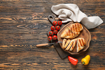 Boards with tasty grilled chicken breast, thyme, tomatoes and bell peppers on wooden background