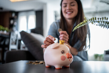 Woman saving money inserting coin in piggy bank at home