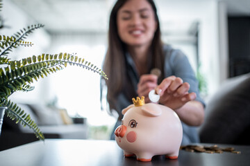 Woman saving money inserting coin in piggy bank at home