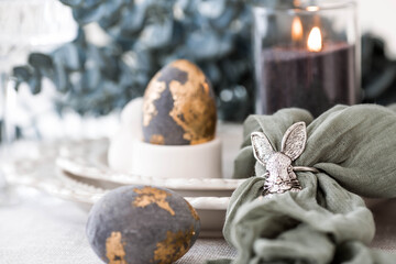 The banner. Table setting. A plate with a rabbit and a napkin, Easter eggs with gilding and a branch of eucalyptus on a linen tablecloth. The concept of a bright Easter holiday.