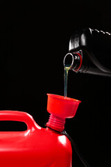 Naklejka premium Pouring of gasoline from bottle into canister on black background, closeup