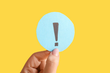 Woman holding paper exclamation mark against yellow background, closeup