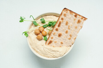 Bowl of delicious hummus with chickpeas, micro green and crispbread on light background