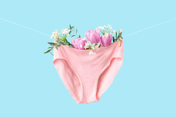 Female panties with flowers hanging on clothesline against blue background