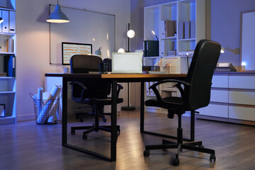 Blank laptop on desk in interior of office at night