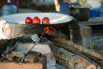 Tomatoes cooking on comal over wood fire in outdoor kitchen