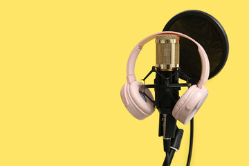 Stand with professional microphone and headphones on yellow background