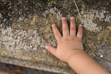 The baby is touching the rock with their hand, and it appears to be a very small baby. The baby's hand is placed on the rock, which could be a stone or a piece of concrete.