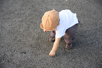 The image shows a small child playing with a toy on the ground, possibly in a park or similar outdoor setting. The child is wearing a hat and appears to be enjoying their time outside.