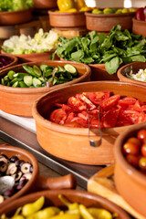 Delicious buffet table with Fresh and Vibrant Organic Vegetables in Rustic Clay Bowls and greens, featuring variety of healthy and colorful plant-based dishes for vegetarian or vegan meal
