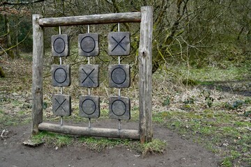 A large rustic wooden noughts and crosses game in a forest location. 