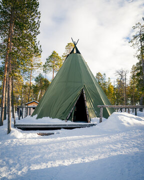 Traditional green Sami style tent known as a lavvu stands peacefully in a snowy forest in Lapland, Finland.  Arctic life and culture. Northern silence