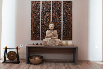 A serene interior featuring a Buddha statue on a wooden table, a carved mandala triptych, candles, bowls, a singing bowl, and a gong in Ischgl, Austria.