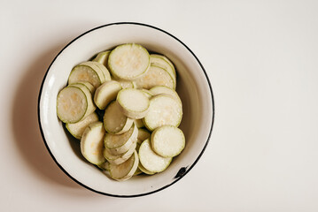 A white bowl filled with sliced ​​fresh zucchini slices on a white background. Perfect for cooking recipes, healthy eating or minimalist style