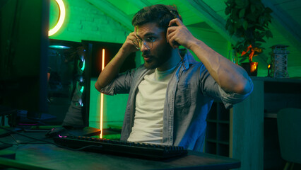Happy Indian man put on headphone talking to microphone start online internet stream vlog blog gaming waving hello greeting computer male Arabian guy radio host work gamer streamer neon night home