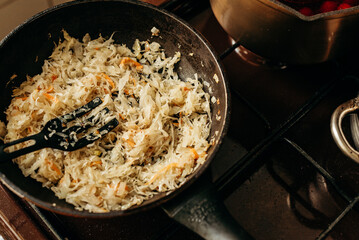 Shredded cabbage and onions are fried in a pan, the shoulder blade is on top. The aromatic dish on the stove creates the atmosphere of home cooking and a warm lunch.