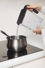 Pouring clean water from filter container into pot on stove for cooking preparation