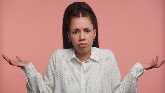 Confused woman shrugging with uncertain expression on pink background