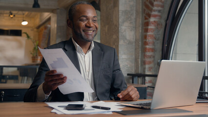 Fototapeta premium African American male manager worker leader in office ethnic businessman man employer talking video call conference negotiate presentation laptop holding papers document business consultation online