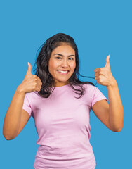 Young latin woman showing thumbs up with both hands and smiling on blue background