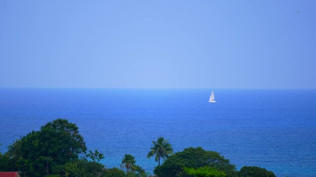 boat crossing ocean towards island. Blue water. White sail