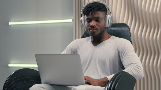Futurism African American man male programmer developer designer cyber data guy in white futuristic room indoors cyberspace modern technology put on wireless headphones open laptop start work online