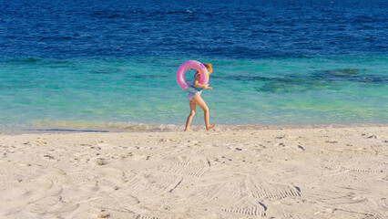 Obraz premium A girl with a swimming ring on the beach. Having fun on vacation at the hotel pool. Colorful vacation concept.
