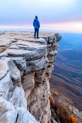 Person gazing at autumn mountain vista from cliff edge