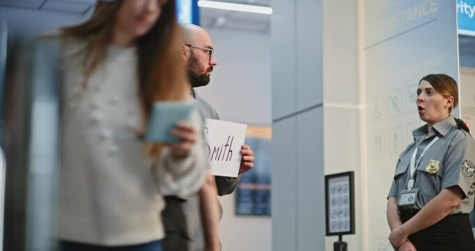 Transportation Service in International Airport Terminal: Airport Greeter Holding Name Sign, Waiting for Passengers From Plane Flight, Talking to Security Officer. Diverse People and Travelers Walking