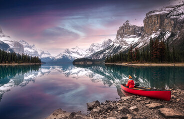 Female traveler in winter coat rowing a red canoe in Spirit Island on Maligne Lake at the sunset