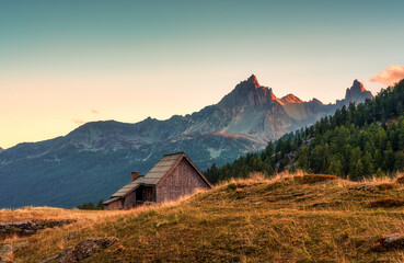 Wooden hut of shepherd on golden meadow and rocky mountain in the evening at Claree valley