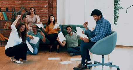 Indian Asian young business professionals, startup partners sitting on floor of modern, cozy office with documents, celebrating success with joyful smiles cheerful expressions