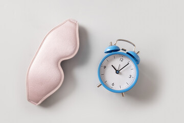 Pink sleeping mask and blue watch, alarm on gray background. Concept of sleep, health care, daily...